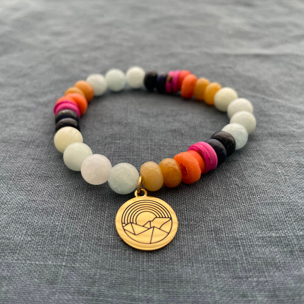 Handmade Colorado Sunset Bracelet featuring Aquamarine, Topaz Jade, Lapis Lazuli, and Blue Sandstone beads, accented with a gold-dipped zinc alloy sunset charm, inspired by Colorado's vibrant sunsets. Handmade in Colorado.